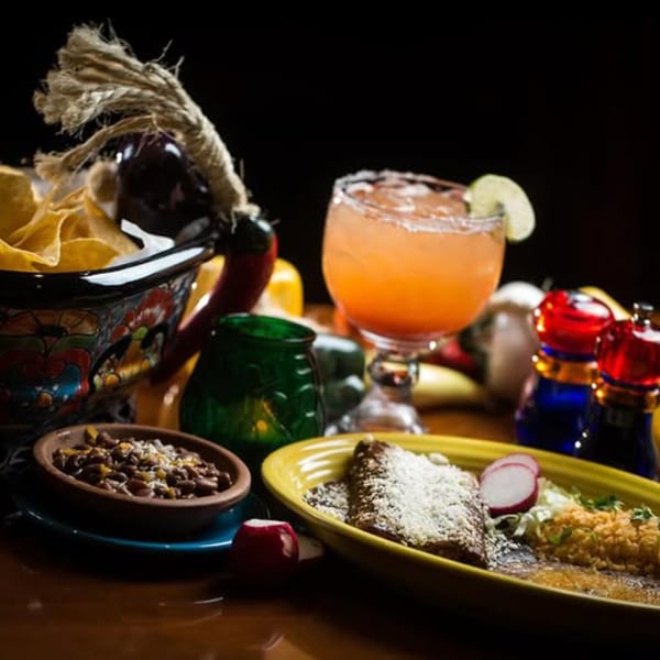 Colorful Mexican meal with tortilla chips, beans, an entree, and a pink margarita.