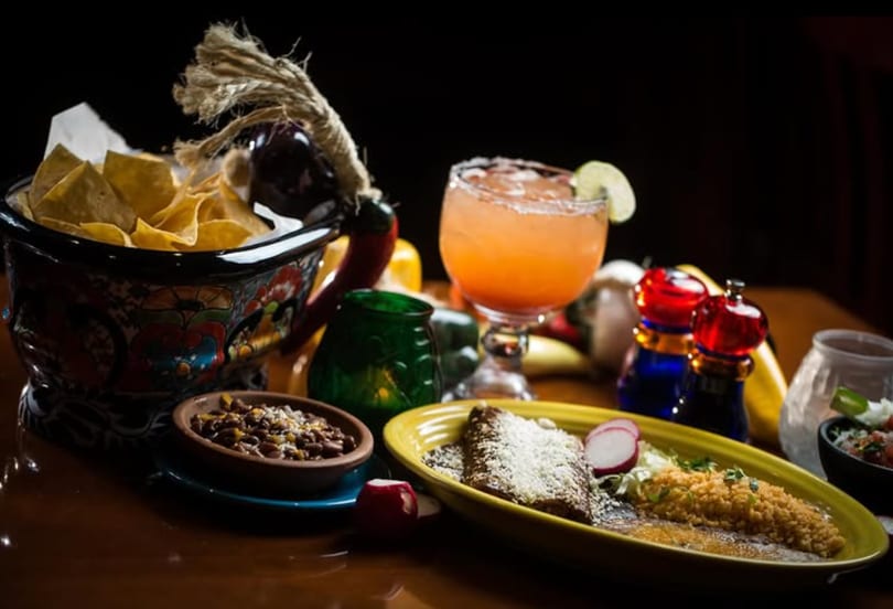 Colorful Mexican meal with tortilla chips, beans, an entree, and a pink margarita.