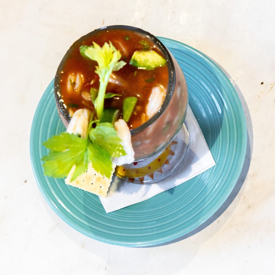 A glass of shrimp ceviche with avocado, celery, and crackers on a vibrant turquoise plate.