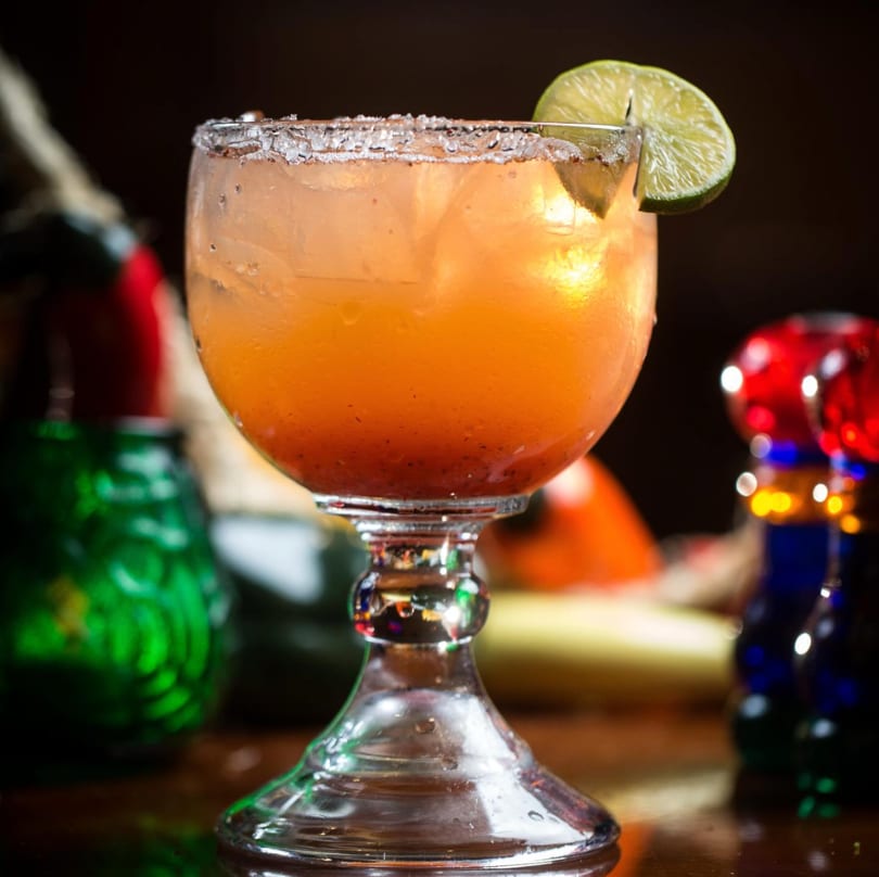 Margarita glass filled with an orange drink, salted rim, and a lime wedge.