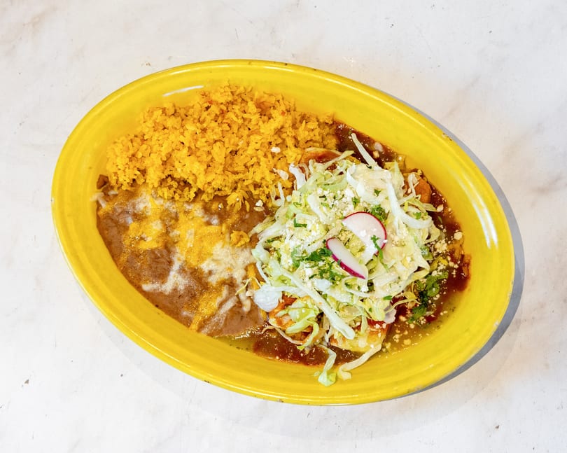 Mexican combo plate with yellow rice, refried beans, and enchiladas topped with lettuce, cheese, and radish.