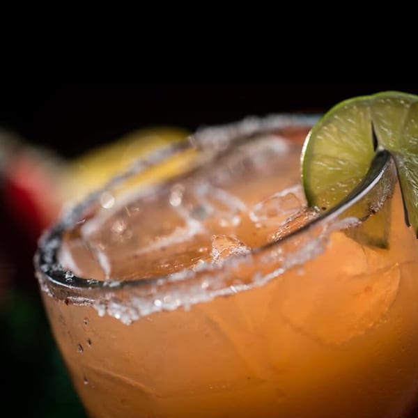 Orange cocktail with ice, a salted rim, and a lime wedge garnish.