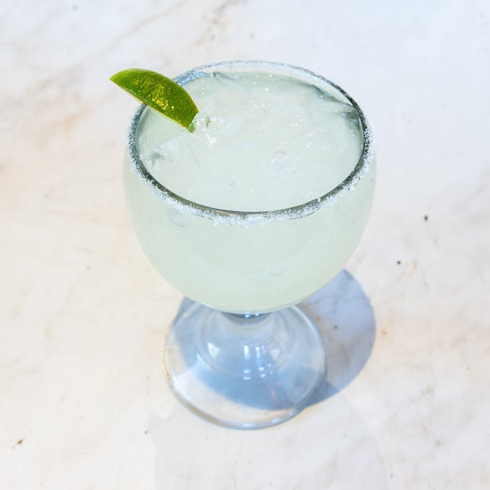 Iced margarita in a goblet glass with a salted rim and lime wedge.