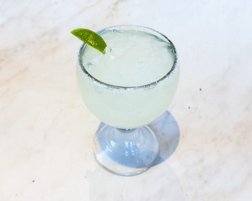 Iced margarita in a goblet glass with a salted rim and lime wedge.