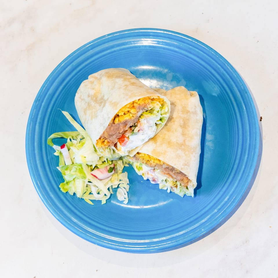 Two halves of a burrito filled with rice, beans, lettuce, and sauce, served on a blue plate with a side salad.