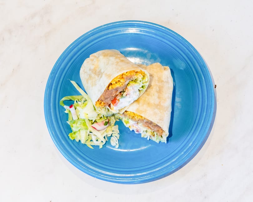 Two halves of a burrito filled with rice, beans, lettuce, and sauce, served on a blue plate with a side salad.