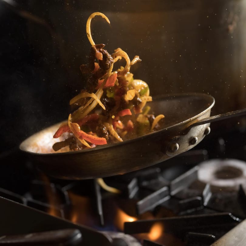 Stir-fry of meat and vegetables tossed in a pan above a flaming gas stove.