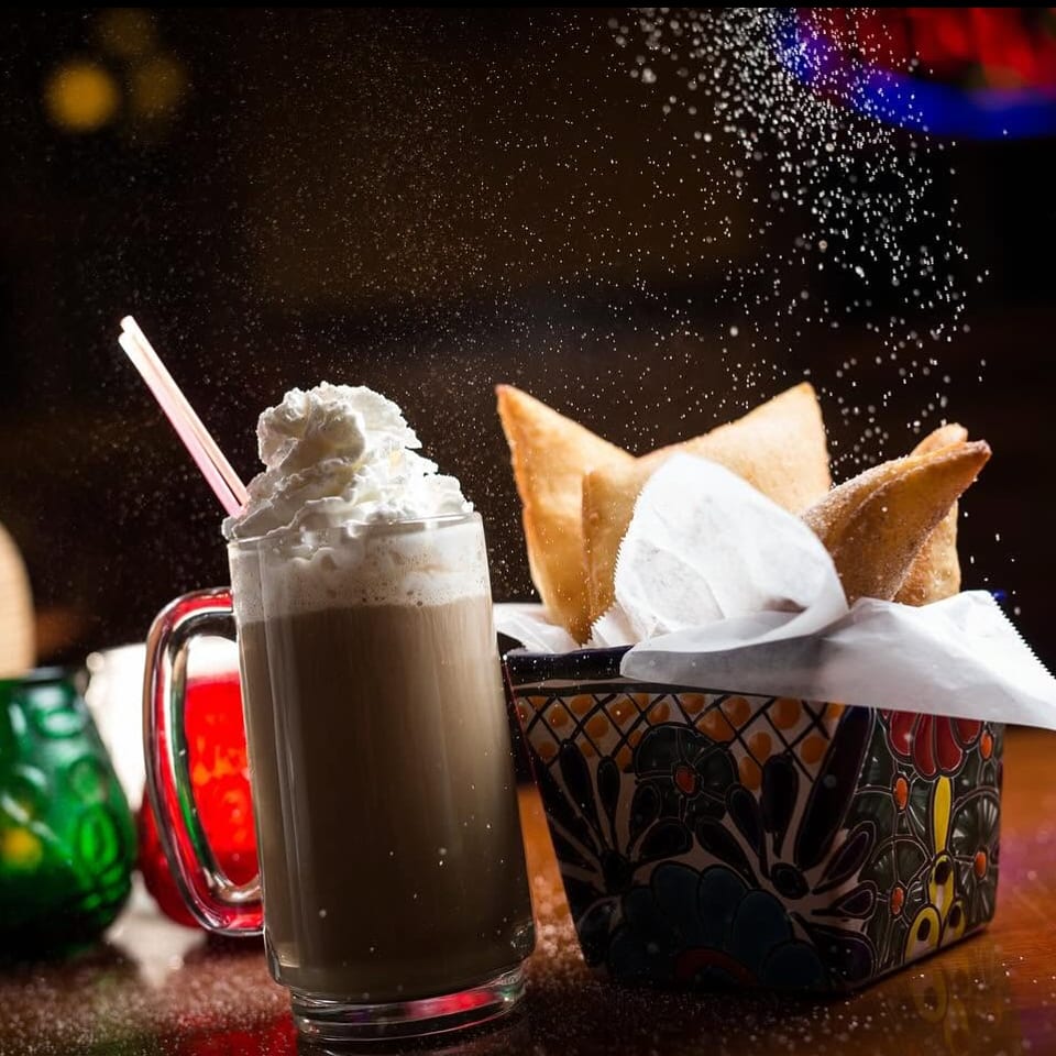 Whipped cream drink and fried pastries in a decorative basket with sugar sprinkling.