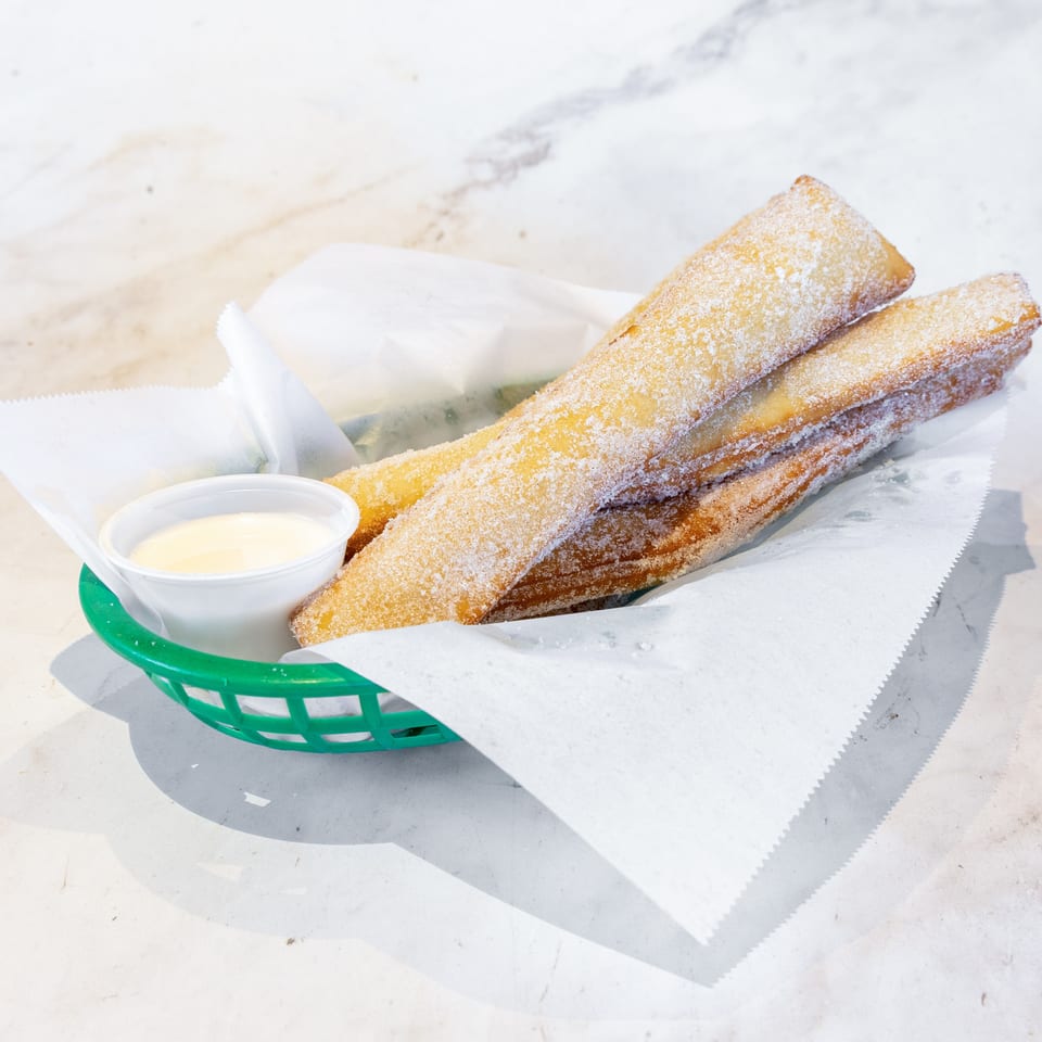 Golden, sugar-coated churros in a green basket with a side of white dipping sauce.