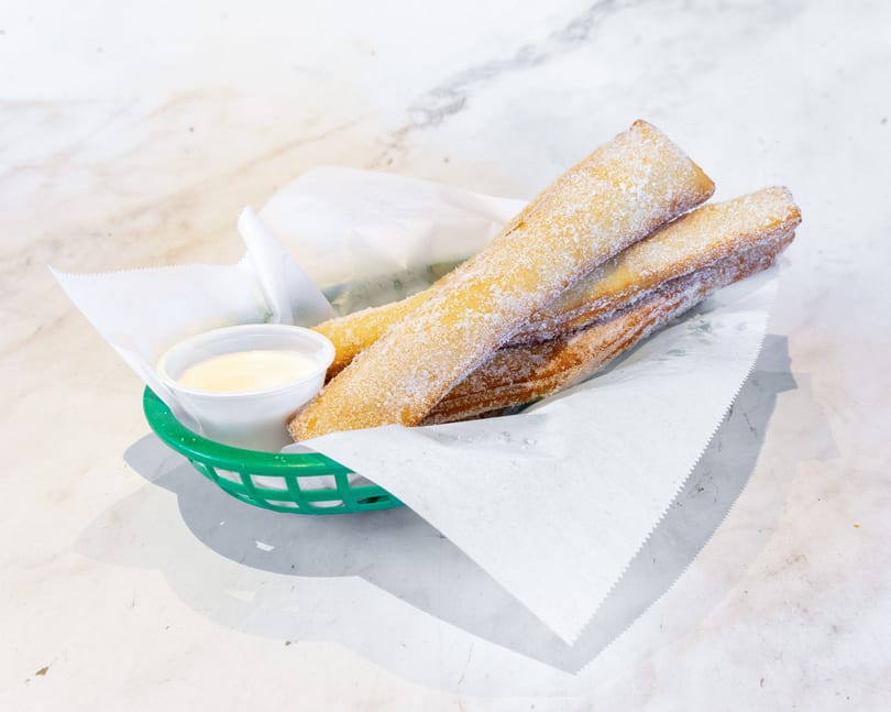 Golden, sugar-coated churros in a green basket with a side of white dipping sauce.