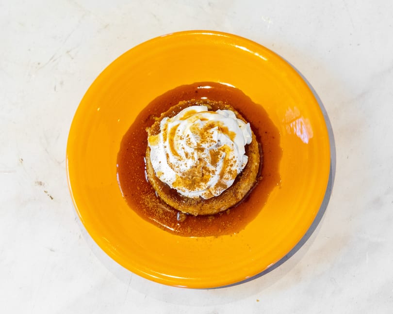 Round dessert with whipped cream, caramel, and cinnamon on a bright orange plate.