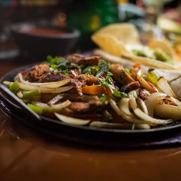 Sizzling plate of chicken fajitas with onions, peppers, tortillas, and shredded cheese.
