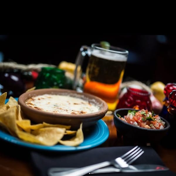 Queso with tortilla chips, pico de gallo, and a beer on a restaurant table.