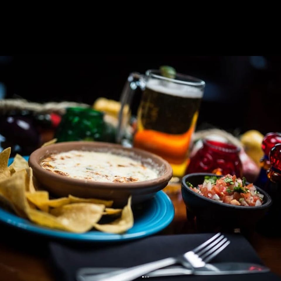 Queso with tortilla chips, pico de gallo, and a beer on a restaurant table.