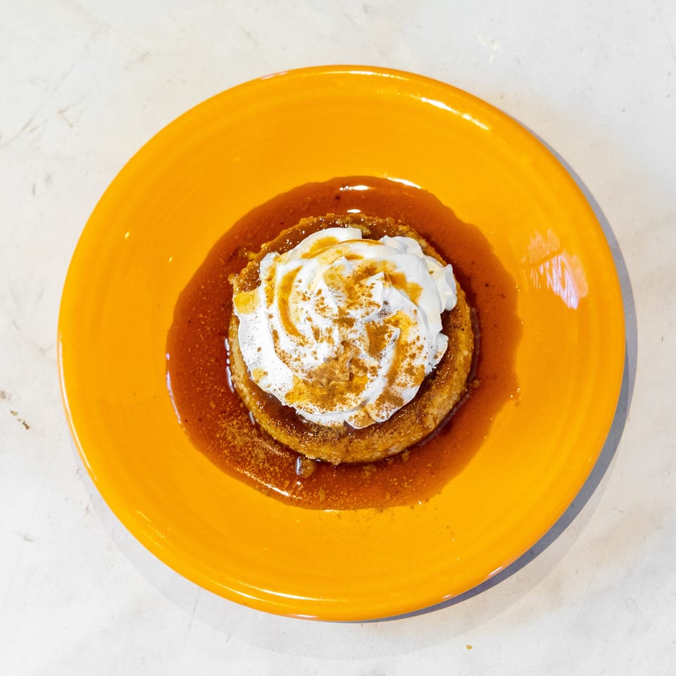 Caramel flan topped with whipped cream and cinnamon on a vibrant orange plate.